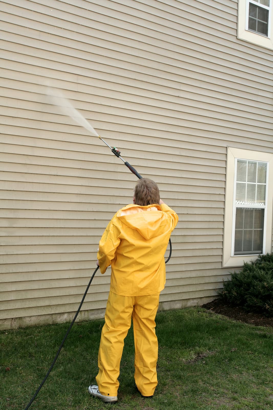 Worker power washing an exterior surface with a pressure washer wand